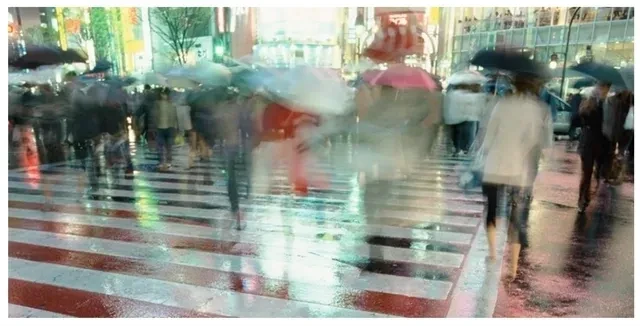 Motion-blurred rainy city crosswalk with pedestrians and umbrellas